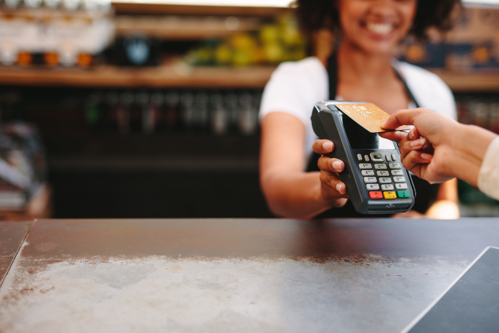 A smiling cashier hands over a payment terminal to a customer for card payment, focusing on the terminal and customer's hand.